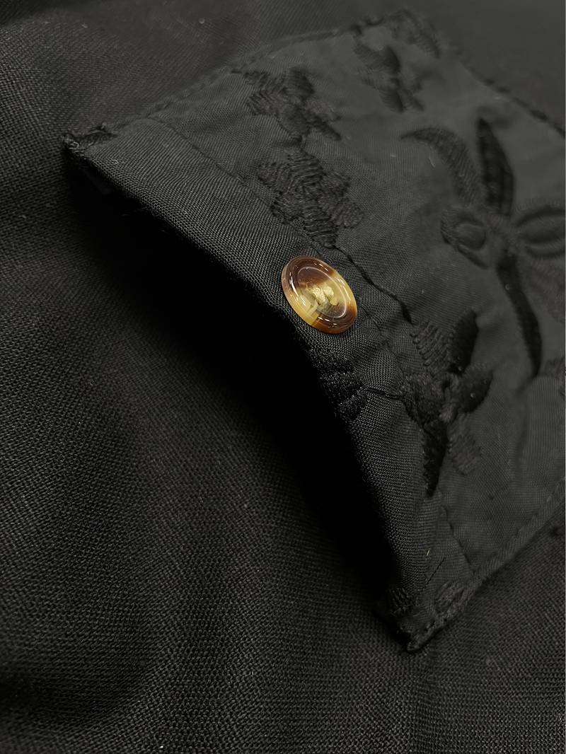 Schwarze Stofftasche mit Knopf, verziert mit floralen Stickereien. Hochwertiges Design, ideal für elegante Mode und Accessoires.