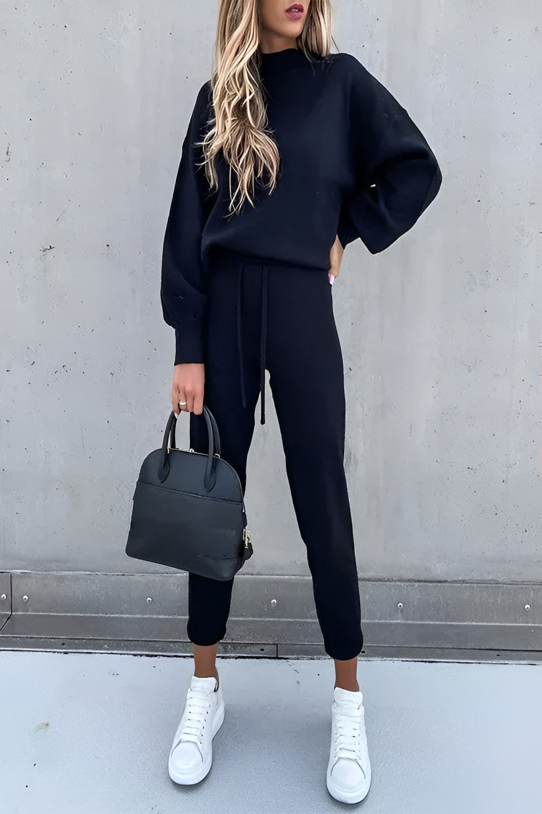 Damen-Sweatshirt und Jogginghose in Schwarz, lässiger Look, kombiniert mit weißen Sneakers und schwarzer Handtasche. Perfekt für Freizeitmode.