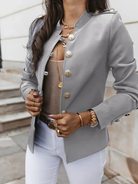 Damenblazer in Grau mit goldenen Knöpfen, kombiniert mit weißer Hose und Schmuck. Elegante Mode, stilvoller Look, trendige Damenbekleidung.