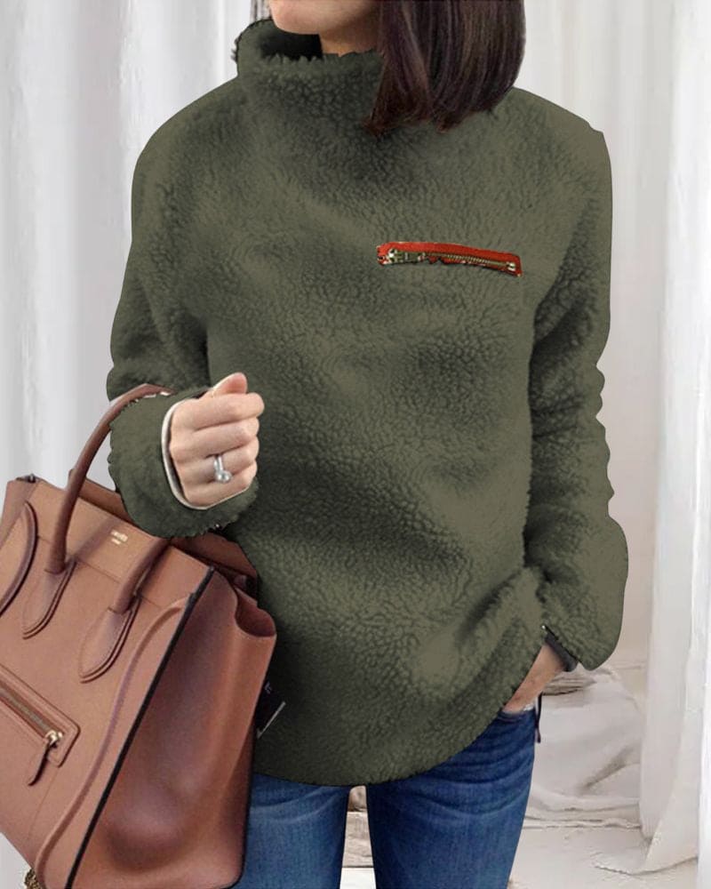 Damen Teddy-Fleece-Pullover in Olivgrün mit hohem Kragen und Reißverschlusstasche, kombiniert mit brauner Lederhandtasche. Wintermode, gemütlich.