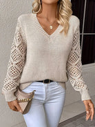 Damenpullover mit V-Ausschnitt, beige, gehäkelte Ärmel, modisch, elegant, ideal für Herbstmode, kombiniert mit weißer Hose und Tasche.