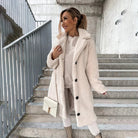 Frau in stilvollem, weichem, aprikosenfarbenem Mantel auf Treppe. Modetrend, Wintermode, Damenbekleidung, eleganter Look, urbaner Stil.