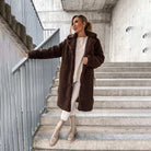 Frau in braunem Teddy-Mantel auf Treppe, modisch und warm. Wintermode, Damenbekleidung, stilvoller Look, Outdoor-Outfit, urbane Eleganz.