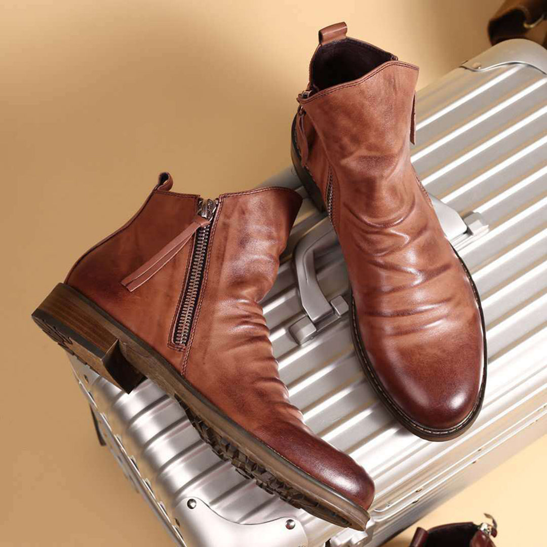 Hochwertige braune Lederstiefel mit Reißverschluss, stilvoll auf silbernem Koffer präsentiert. Perfekt für Herrenmode und Herbsttrends.