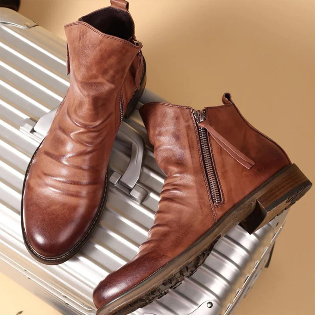 Hochwertige braune Lederstiefel mit Reißverschluss auf silbernem Koffer. Stilvolle Herrenmode, ideal für Reisen und urbane Abenteuer.