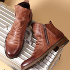 Hochwertige braune Lederstiefel mit Reißverschluss auf silbernem Koffer. Stilvolle Herrenmode, ideal für Reisen und urbane Abenteuer.