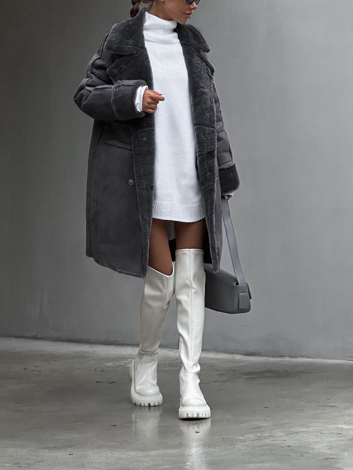 Frau in grauem Mantel und weißem Strickkleid, kombiniert mit weißen Overknee-Stiefeln und grauer Handtasche. Modetrend Herbst/Winter 2023.