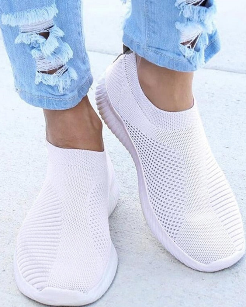 Weiße, atmungsaktive Sneaker aus Strickmaterial, kombiniert mit zerrissenen Jeans. Modische, bequeme Schuhe für Damen, ideal für den Alltag.