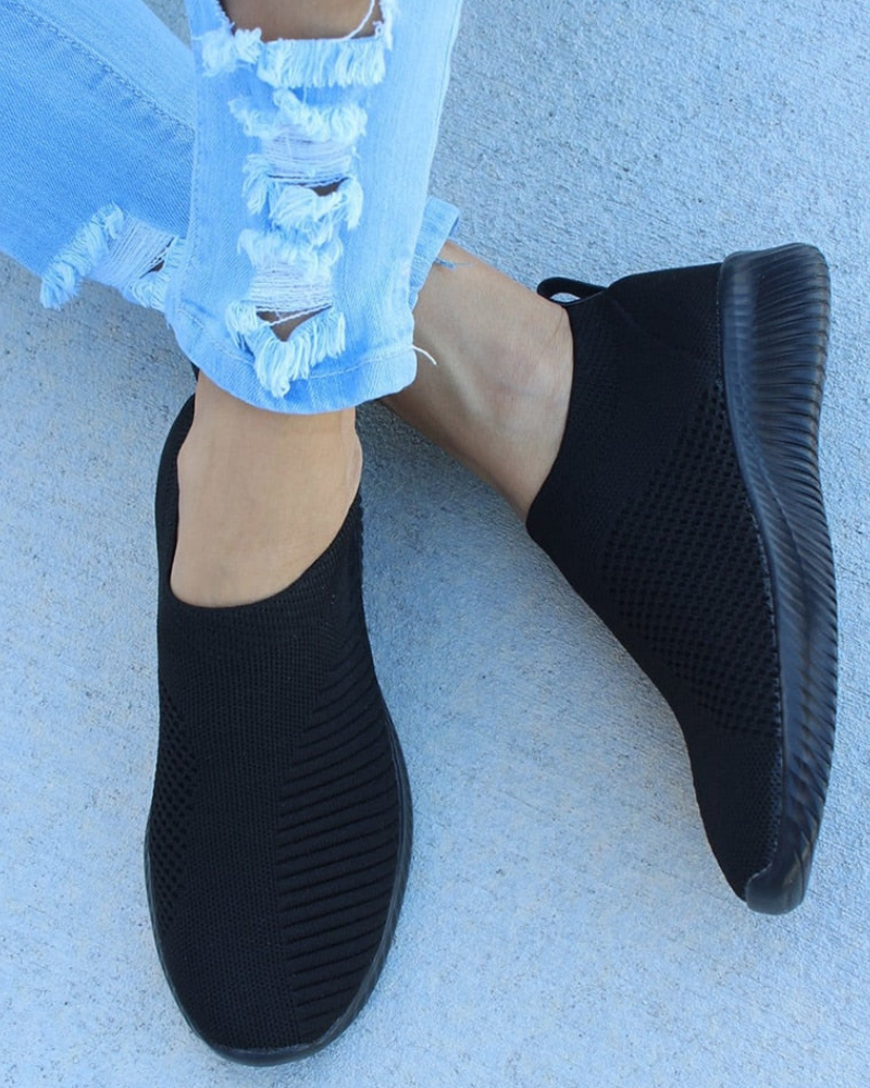Schwarze Slip-On-Sneaker aus atmungsaktivem Strickmaterial, kombiniert mit zerrissenen Jeans. Bequeme Freizeitschuhe für Damen.