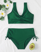 Dunkelgrüner Bikini-Set mit hoher Taille, V-Ausschnitt, Blumen und Avocado-Dekor auf weißem Hintergrund.