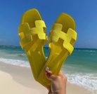 Gelbe Sandalen am Strand vor blauem Meer und Himmel. Perfekt für Sommermode, Strandurlaub und stilvolle Freizeitkleidung.