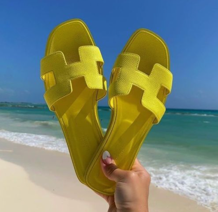 Gelbe Sandalen am Strand vor blauem Meer und Himmel. Perfekt für Sommermode, Strandurlaub und stilvolle Freizeitkleidung.