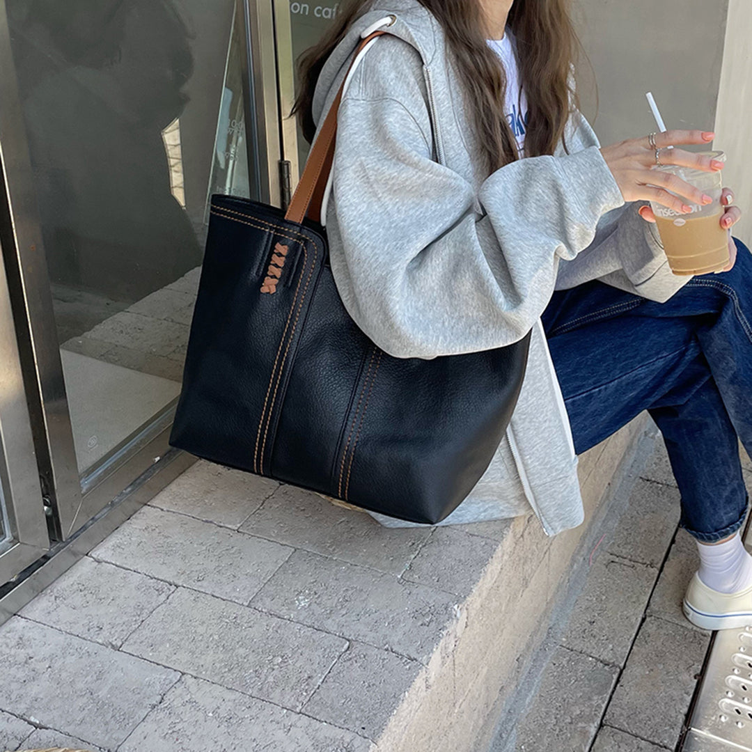 Damenhandtasche aus schwarzem Leder mit braunen Nähten, lässig kombiniert mit Jeans und grauem Hoodie. Perfekt für stilvolle Alltagslooks.