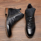 Schwarze Lederstiefeletten mit seitlichem Reißverschluss auf Holzboden. Elegante Damenstiefel, ideal für Herbstmode. Hochwertige Verarbeitung.