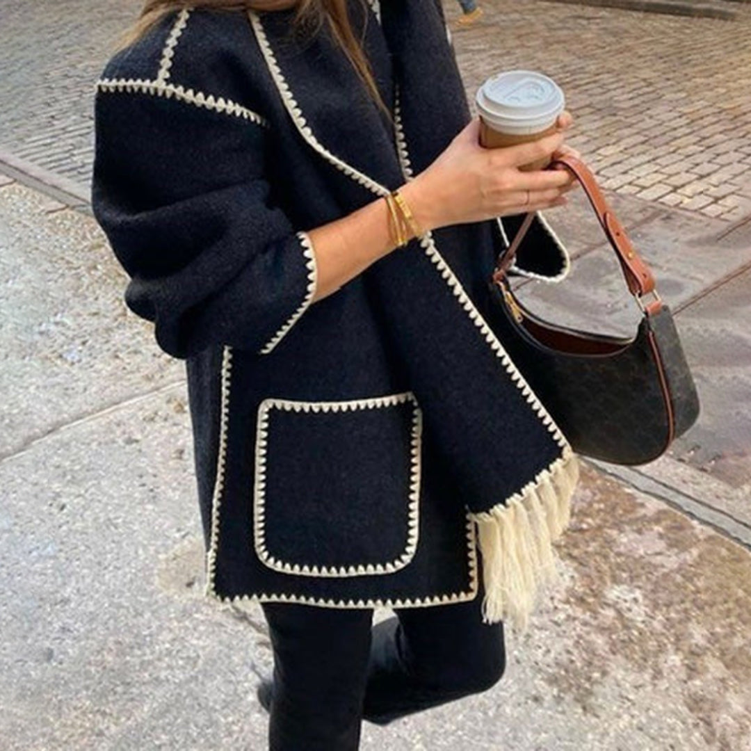 Frau in schwarzem Mantel mit weißen Nähten, hält Kaffeebecher und Handtasche. Modetrend, Herbstmode, stilvoller Look, Straßenmode.