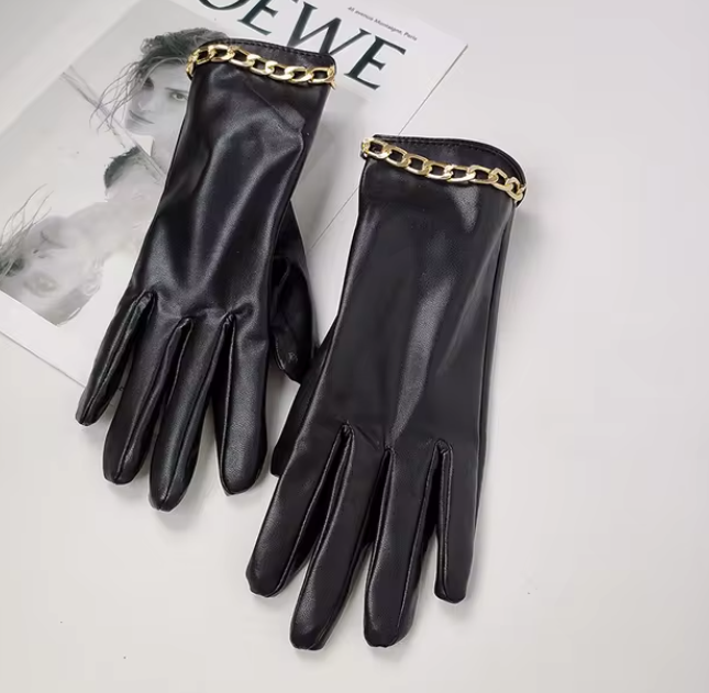 Schwarze Lederhandschuhe mit goldener Kettenverzierung auf weißem Hintergrund, stilvoll und elegant, ideal für modische Herbst- und Winteroutfits.