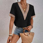 Schwarze Damenbluse mit V-Ausschnitt und Spitzenbesatz, kombiniert mit Jeansshorts und Strohtasche. Perfekt für Sommermode und Freizeitlook.