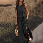 Frau in schwarzem ärmellosen Sommerkleid, Strohhut, Sandalen, mit Strohtasche auf Landstraße.