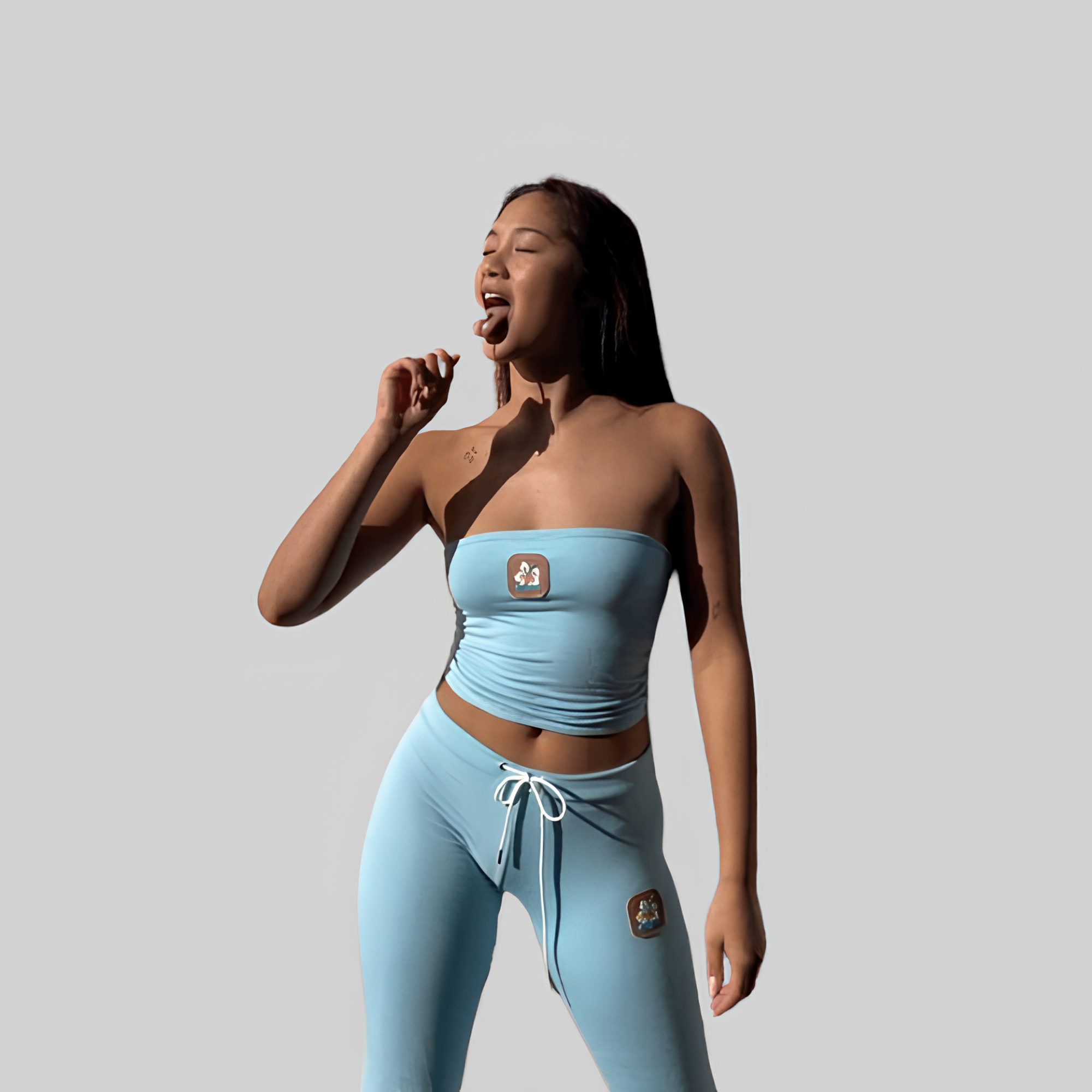 Frau in hellblauem Sportoutfit, bestehend aus trägerlosem Top und Leggings, vor grauem Hintergrund. Fitnessmode, trendige Sportbekleidung.