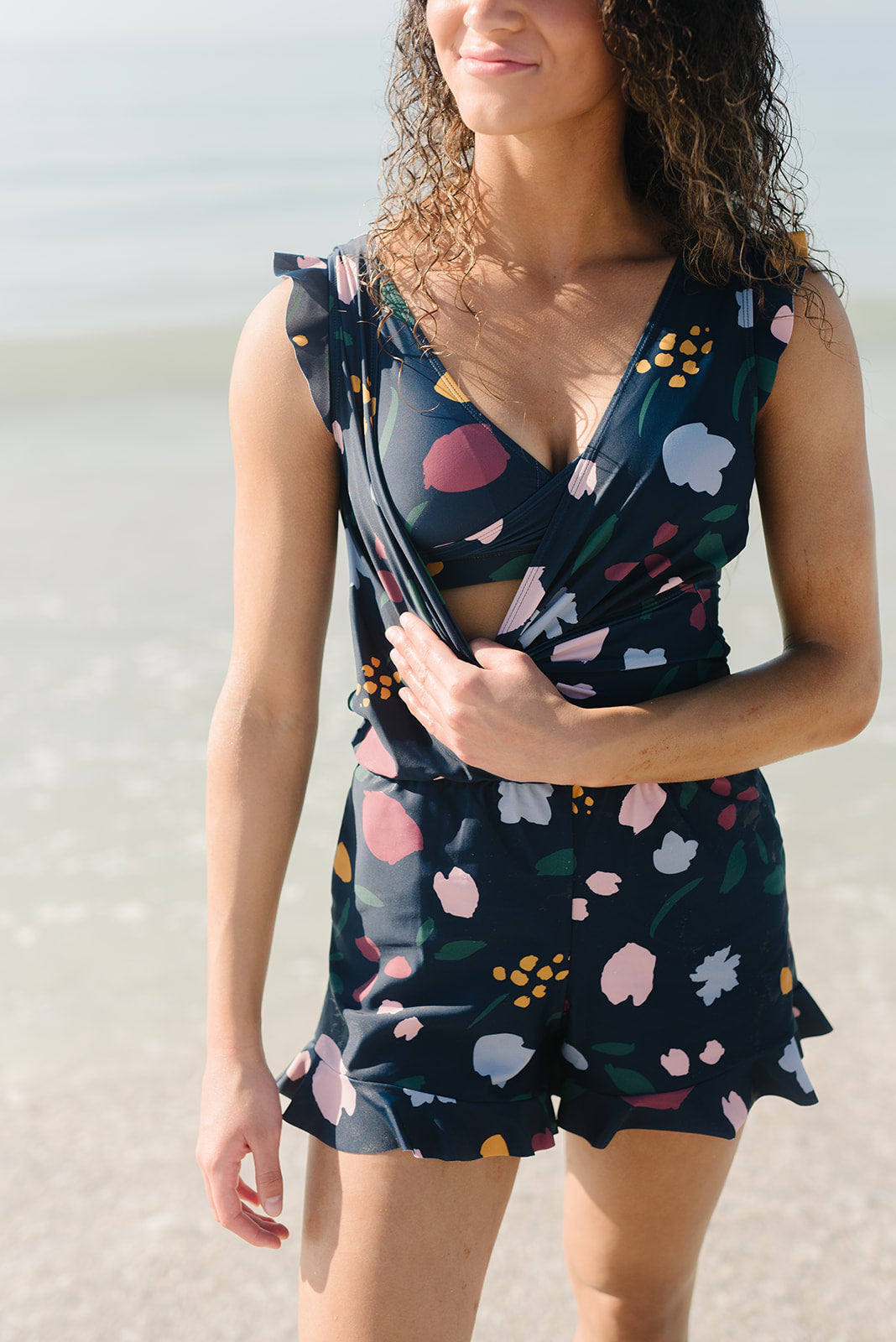 Frau im geblümten Badeanzug-Romper am Strand, dunkelblau, integrierter BH, Sommermode.