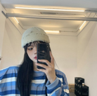 Junge Frau mit gestreiftem Pullover und Mütze macht Selfie im modernen Raum. Mode, Streetwear, Selfie, trendige Kleidung, urbaner Stil.