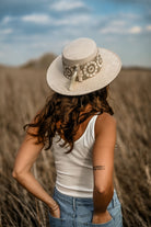 Frau mit weißem Hut und Stickerei, steht in einem Feld. Sommermode, Boho-Stil, Freizeitkleidung, Natur, Outdoor-Fotografie.
