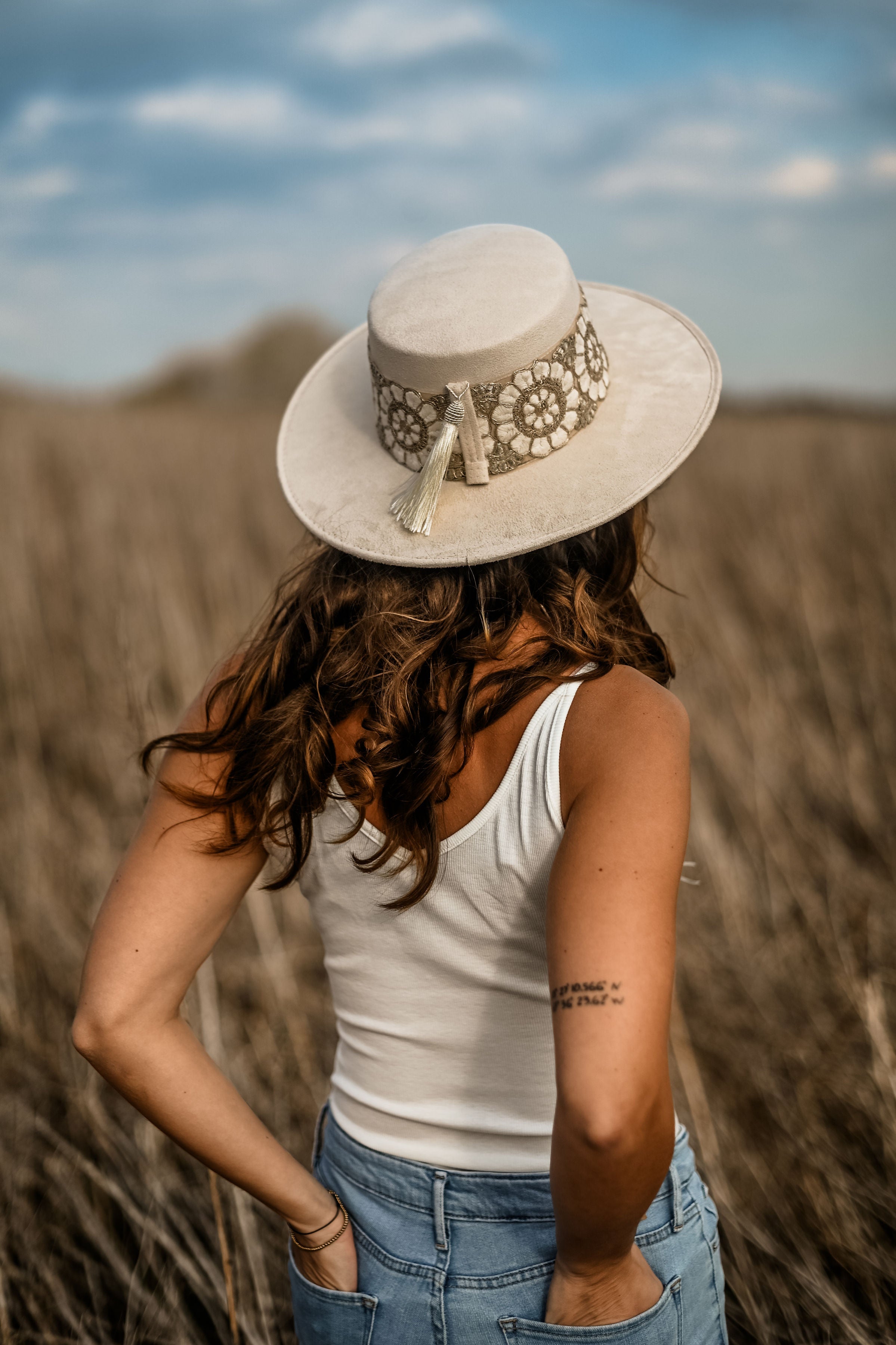 Frau mit weißem Hut und Stickerei, steht in einem Feld. Sommermode, Boho-Stil, Freizeitkleidung, Natur, Outdoor-Fotografie.