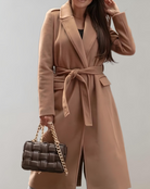 Damenmantel in Kamelhaarfarbe mit Gürtel, kombiniert mit einer eleganten, geflochtenen Handtasche aus Leder mit goldener Kette. Perfekt für Herbstmode.
