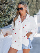Weiße Damenbluse mit roten Herzstickereien, lässig und locker geschnitten, ideal für Frühling 2023. Perfekt für modische Freizeitoutfits.