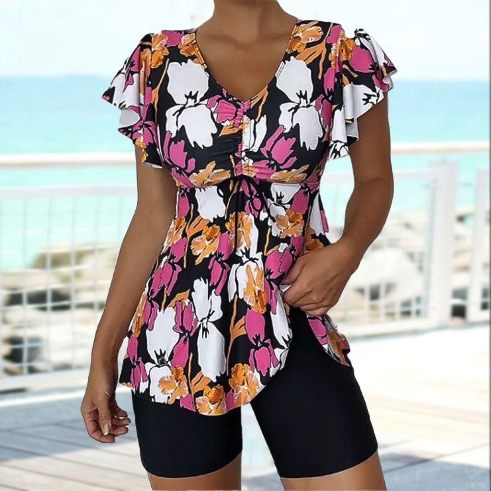 Feminines Sommeroutfit: Blumige Tunika mit Rüschenärmeln und V-Ausschnitt, kombiniert mit schwarzen Shorts. Perfekt für Strand und Freizeit.
