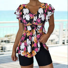 Feminines Sommeroutfit: Blumige Tunika mit Rüschenärmeln und V-Ausschnitt, kombiniert mit schwarzen Shorts. Perfekt für Strand und Freizeit.