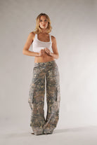 Frau in Camouflage-Cargohose und weißem Tanktop. Modetrend, lässiger Stil, Outdoor-Look, Damenbekleidung, bequeme Freizeitmode.