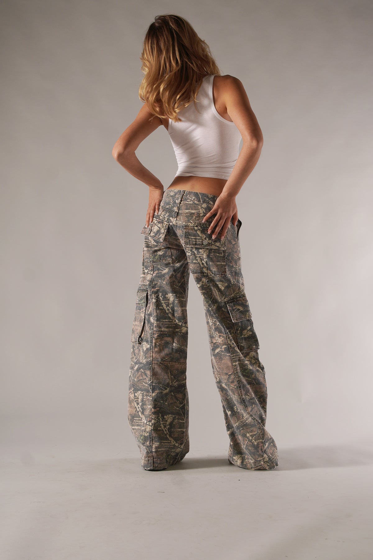 Frau in weißem Tanktop und Camouflage-Cargohose, modisch und lässig. Perfekt für Streetwear, Outdoor-Abenteuer und trendige Freizeitlooks.