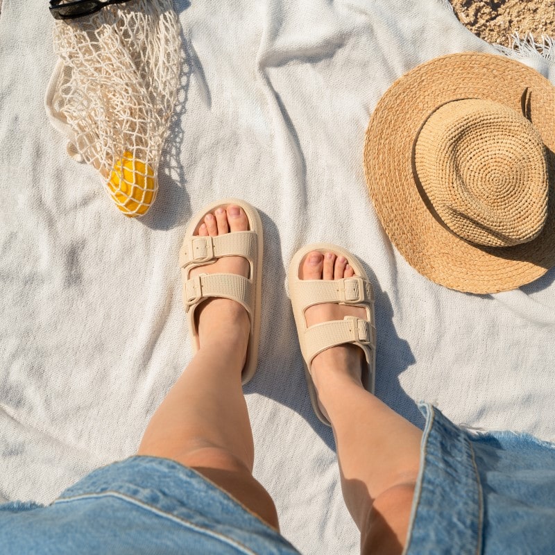 Beige Sandalen auf Stranddecke, Strohhut und Netz mit Zitrone. Sommermode, Strandaccessoires, bequeme Schuhe, Urlaubsoutfit.
