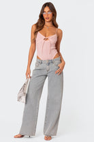 Frau in rosa Top und weiten Jeans, trägt silberne Tasche und Sonnenbrille. Modetrends 2023, lässiger Look, Damenmode, Streetstyle.
