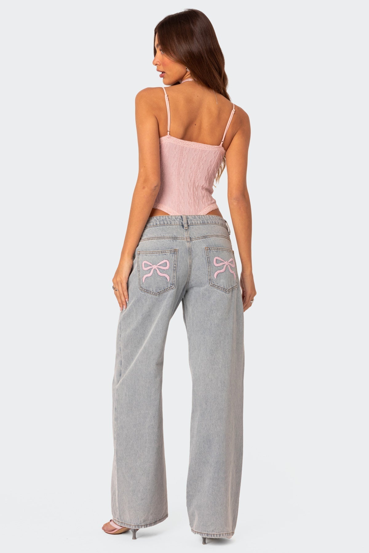 Frau in rosa Top und weiten Jeans mit Schleifenstickerei, modisch und lässig. Perfekt für trendige Streetwear und Sommermode.