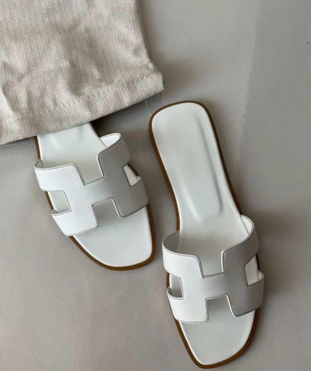Weiße Sandalen mit breitem Riemen und flachem Absatz auf grauem Hintergrund. Modische Sommerschuhe, ideal für Damen.
