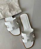Weiße Sandalen mit breitem Riemen und flachem Absatz auf grauem Hintergrund. Modische Sommerschuhe, ideal für Damen.
