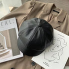 Schwarze Leder-Newsboy-Mütze auf beigem Mantel, stilvoll und modern. Perfekt für Herbst und Winter. Trendige Damenmode, koreanischer Stil.