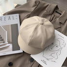 Beige Leder-Newsboy-Cap auf braunem Mantel, stilvoll und modern. Perfekt für Herbst und Winter. Hochwertige PU-Leder, koreanisches Design.