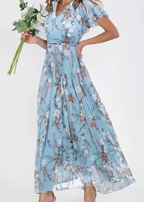 Frau in blauem, geblümtem Maxikleid mit Blumenstrauß, elegantes Sommeroutfit.