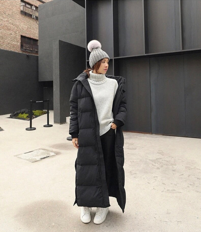 Frau in langem schwarzen Daunenmantel, grauem Rollkragenpullover und Mütze mit Bommel. Wintermode, urbaner Stil, warme Kleidung.