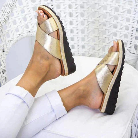 Goldene Sandalen mit Kreuzriemen und schwarzer Sohle, ideal für Sommermode. Bequeme Damen-Slipper, perfekt für Strand und Freizeit.