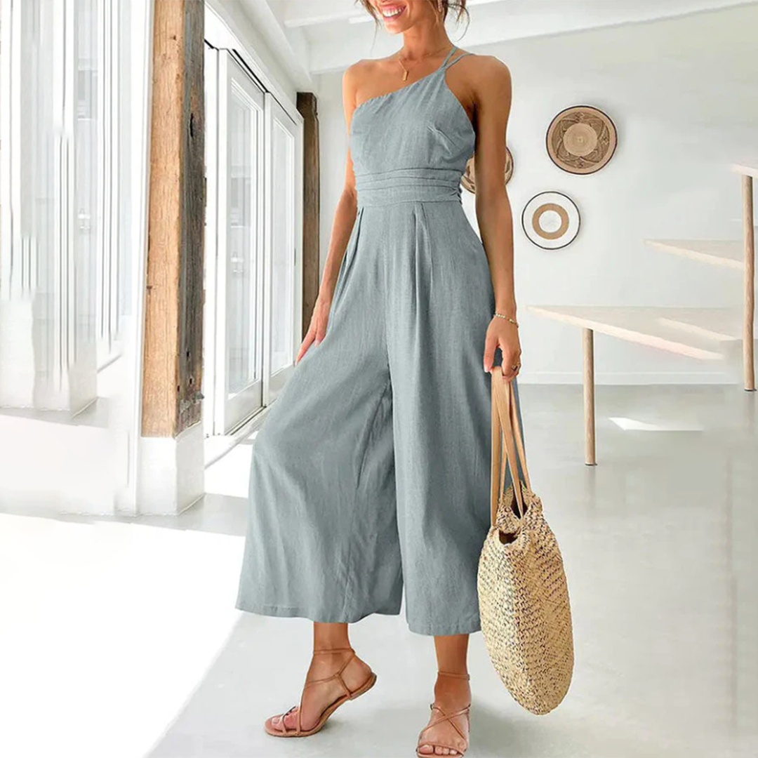 Frau in grauem Jumpsuit mit Strohtasche, Sommermode, elegantes Design, helle Umgebung.