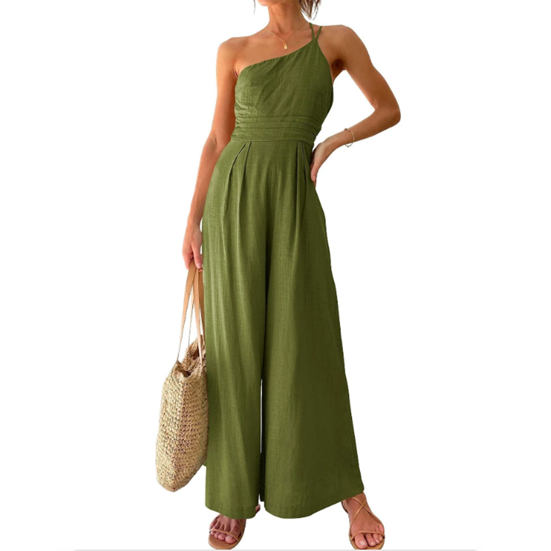 Frau in grünem, schulterfreiem Jumpsuit aus Leinen mit Strohtasche und Sandalen.