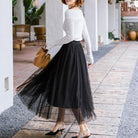 Frau in elegantem, schwarzem Tüllrock und weißem Oberteil, trägt braune Handtasche. Modetrend, Damenmode, stilvoller Look, Streetstyle.