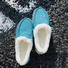 Blaue Hausschuhe mit weißem Plüschfutter auf Asphalt. Bequeme, warme Pantoffeln für Damen und Herren. Ideal für kalte Wintertage.