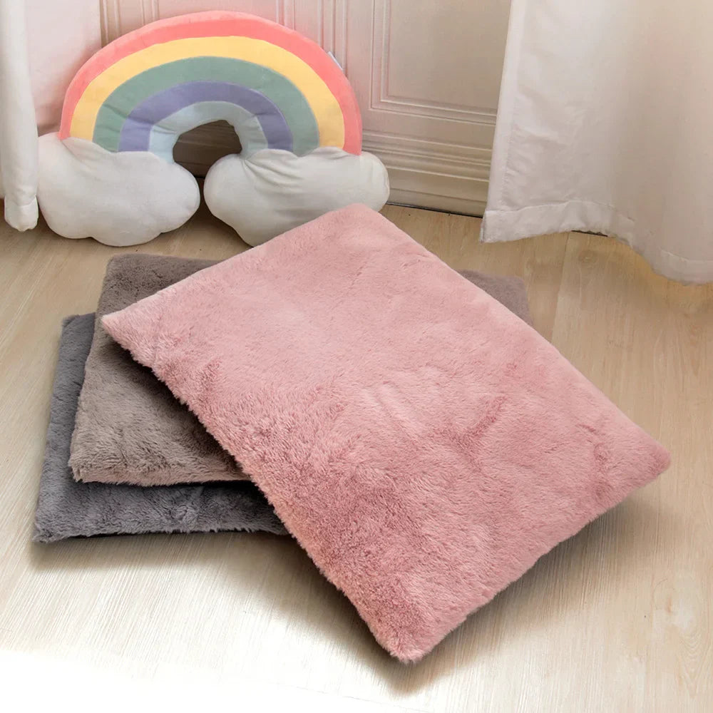 Rosa und graue Plüschkissen auf Holzboden vor Regenbogen-Dekoration.