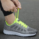 Grauer Sportschuh mit neongelben Schnürsenkeln auf Asphalt. Atmungsaktives Mesh-Design, ideal für Laufen und Fitness. Trendige Herrenmode.