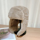 Kuschelige, beige Wintermütze aus Kunstpelz mit Ohrenklappen auf einem Tisch. Perfekt für kalte Tage, modisch und warm. Ideal für Wintermode.